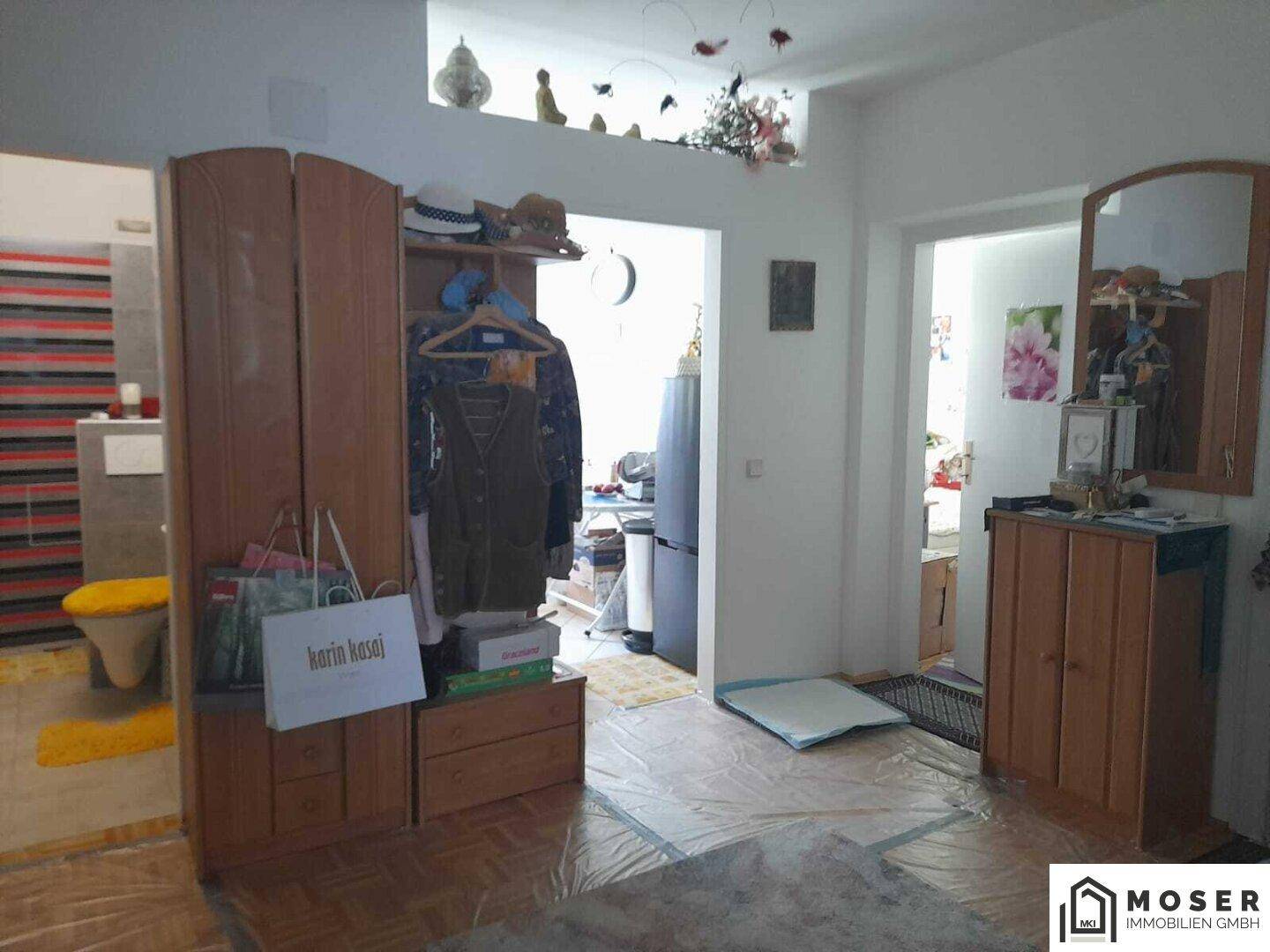 Eingangsbereich mit Holzschrank, Spiegel und Blick in angrenzende, hell beleuchtete Räume.