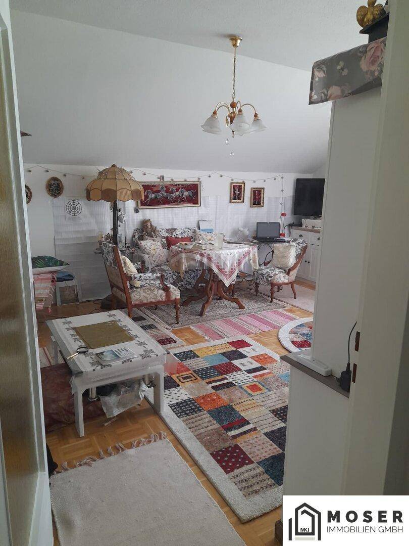 Gemütliches Wohnzimmer mit Holzboden, Esstisch und bunten Teppichen, offen gestaltet.