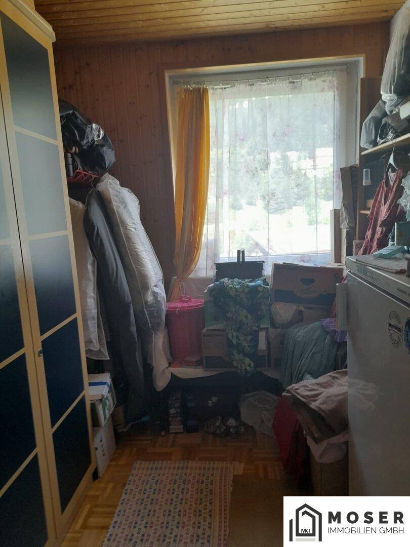 Kleiner Abstellraum oder Zimmer mit Holzverkleidung, Fenster und viel Stauraum für diverse Gegenstände.