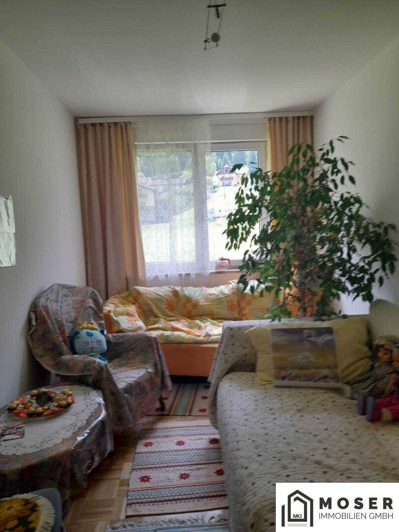 Helles Zimmer mit Fenster, Sofa und Pflanzen, das als Schlaf- oder Gästezimmer genutzt werden könnte.