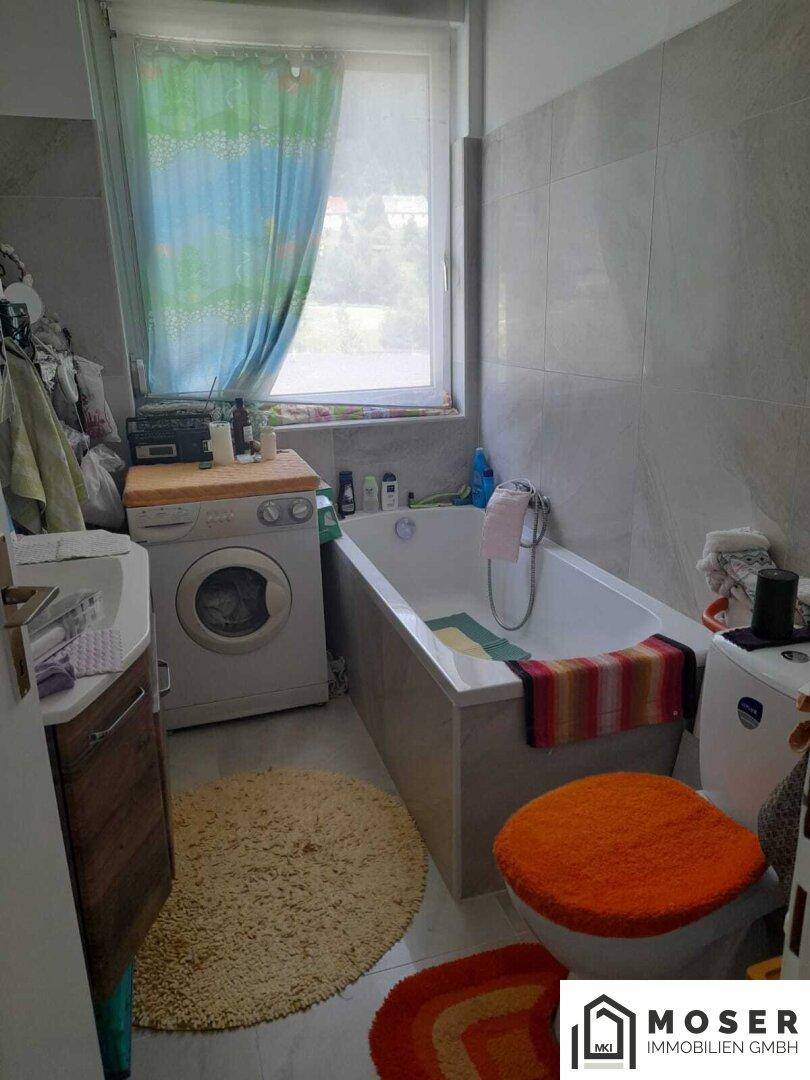 Badezimmer mit Badewanne, Waschmaschine, Toilette und Fenster, hell und funktional eingerichtet.