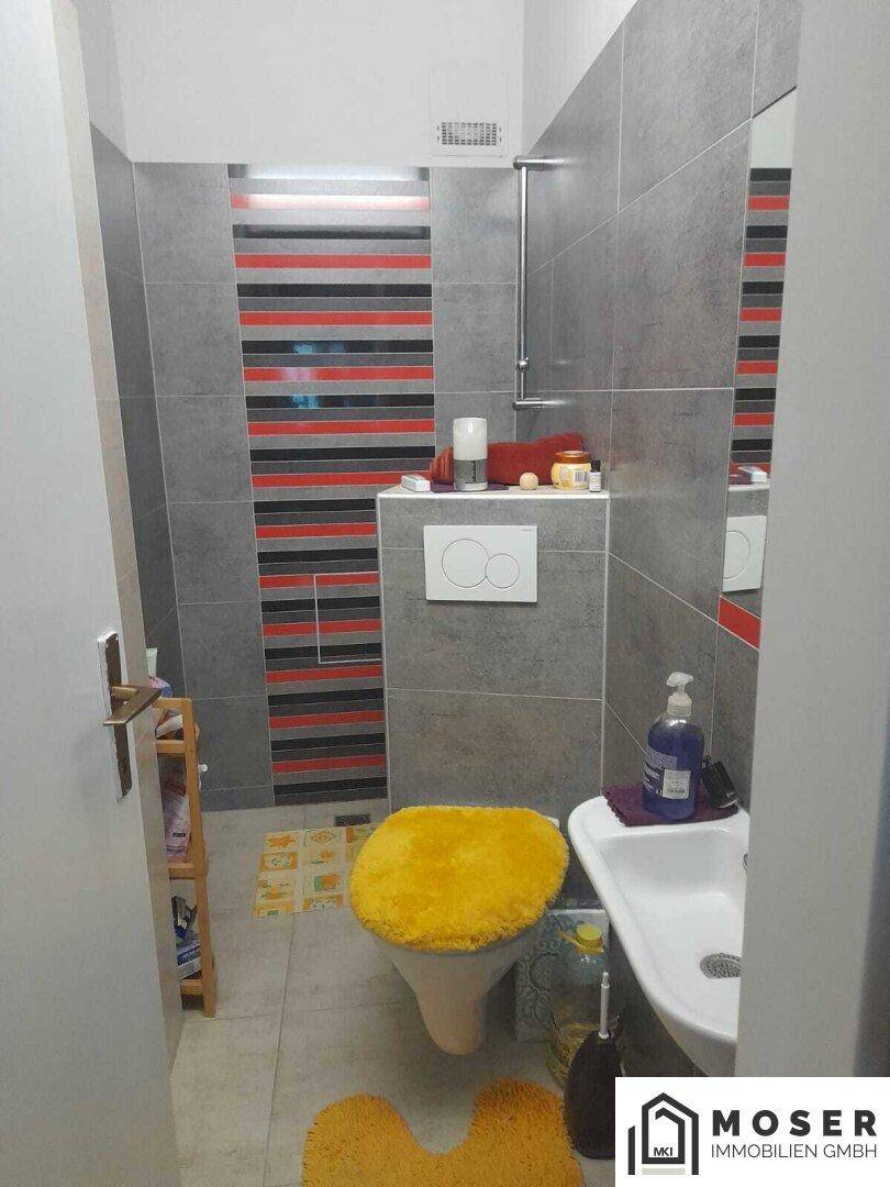 Kleines WC mit modernen grauen Fliesen und farbigen Akzentstreifen, ausgestattet mit Wand-WC.