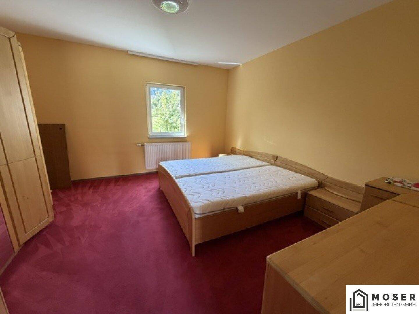 Gemütliches Schlafzimmer mit Doppelbett, Holzmöbeln und rotem Teppichboden, hell und freundlich.