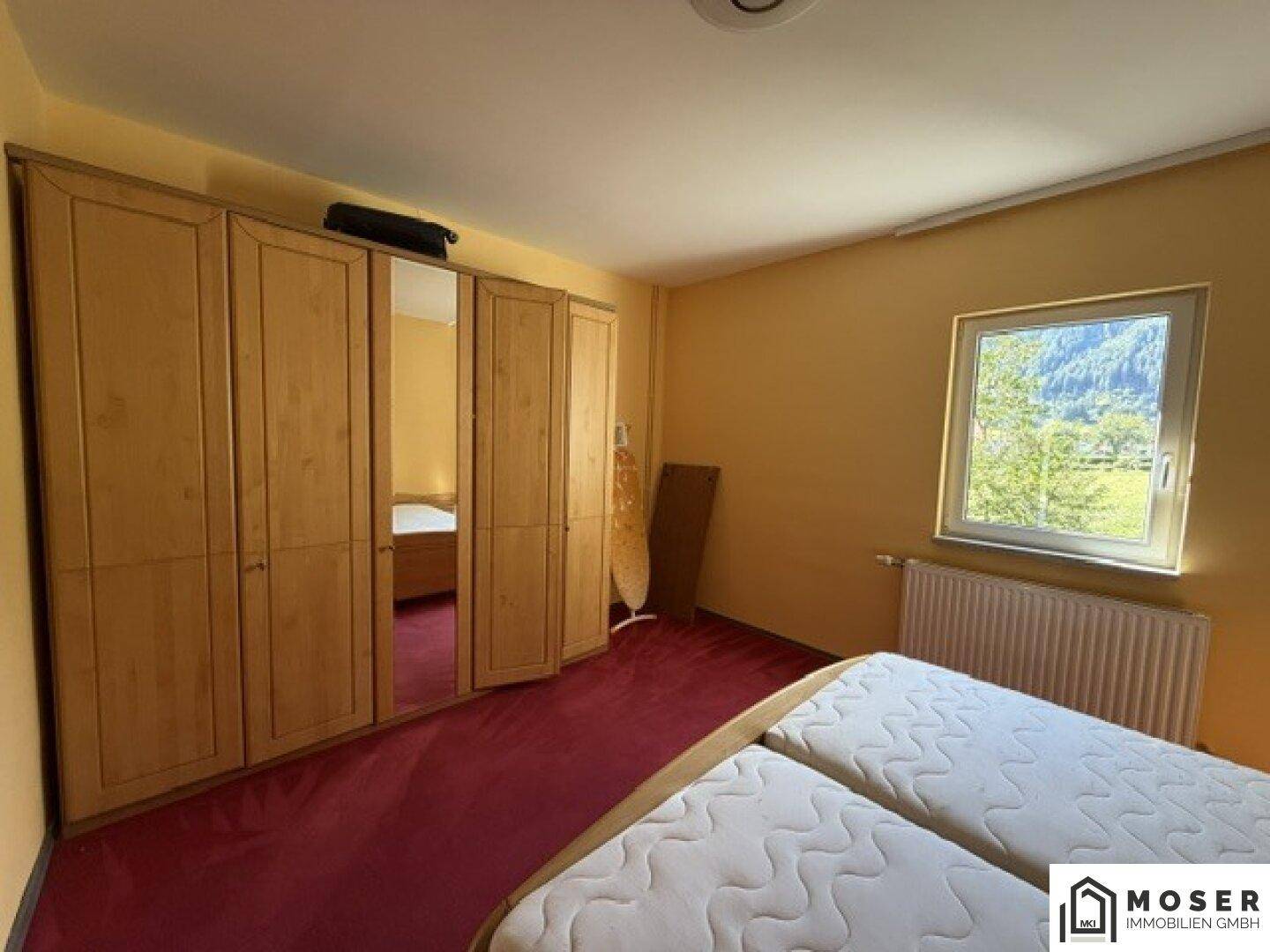 Schlafzimmer mit großem Holzschrank, Spiegeltüren und Blick auf die grüne Landschaft.