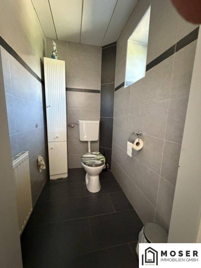 Separates WC mit Toilette, schmalem Schrank und modernen grauen Fliesen, funktional und sauber.