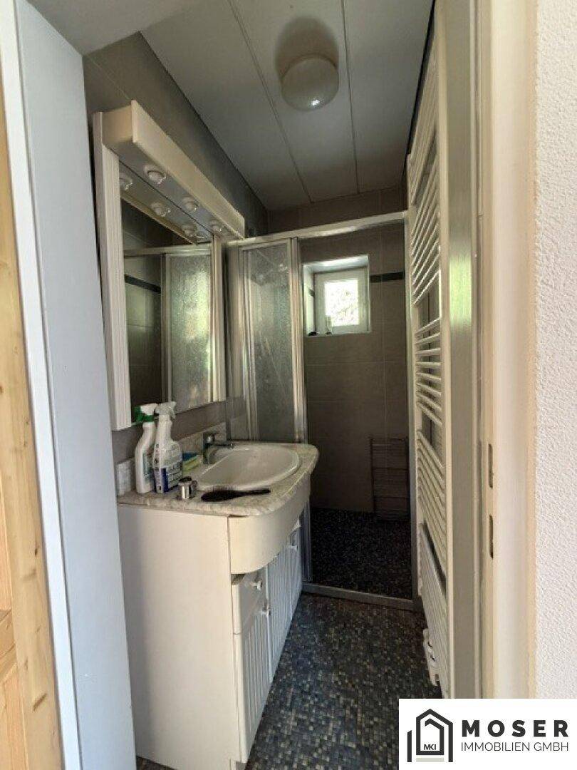 Badezimmer mit Waschbecken, Spiegelschrank, Duschkabine und Handtuchheizkörper, mit Fenster.