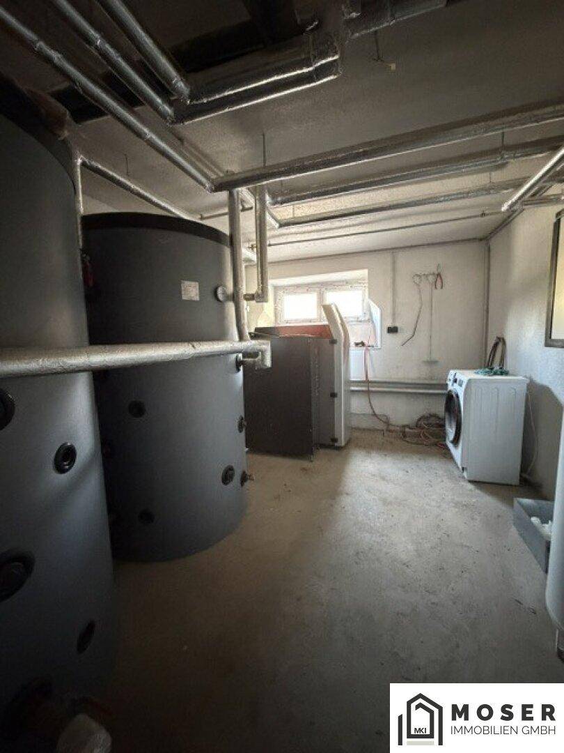 Heizungsraum mit großen Wassertanks, Rohrleitungen und einer Waschmaschine, gut organisiert.