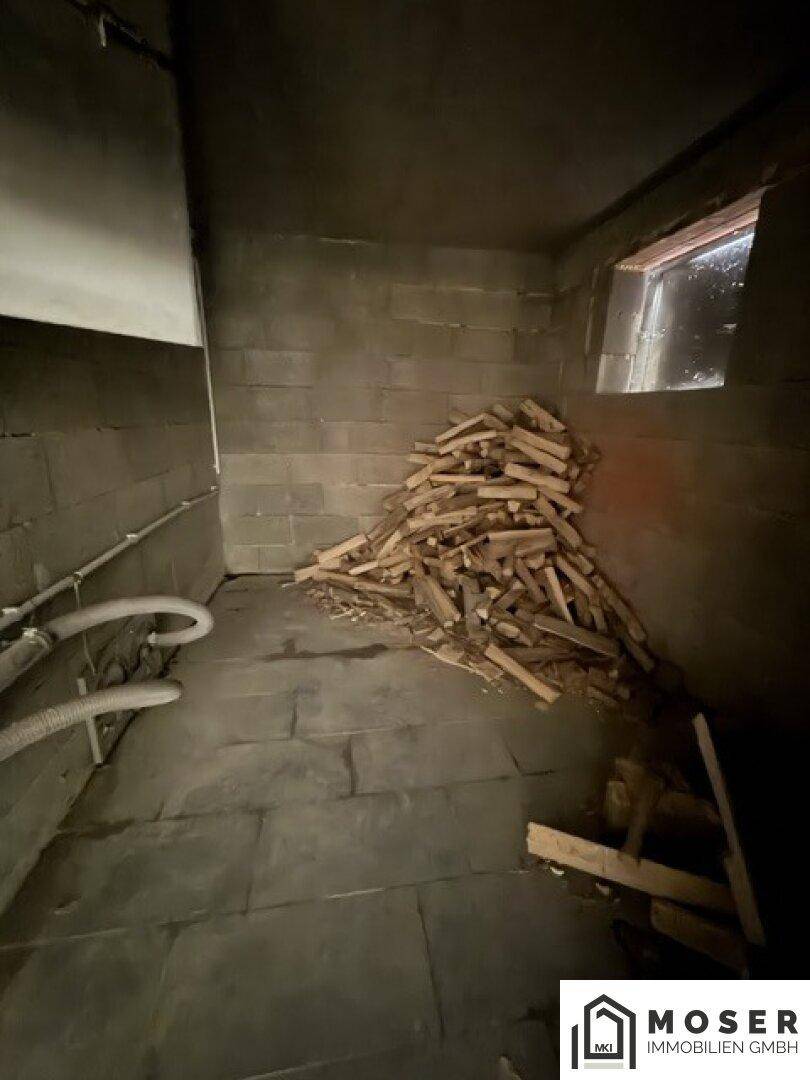 Dunkler Lagerraum mit Betonwänden und einem Stapel Brennholz, praktisch für den Winter.