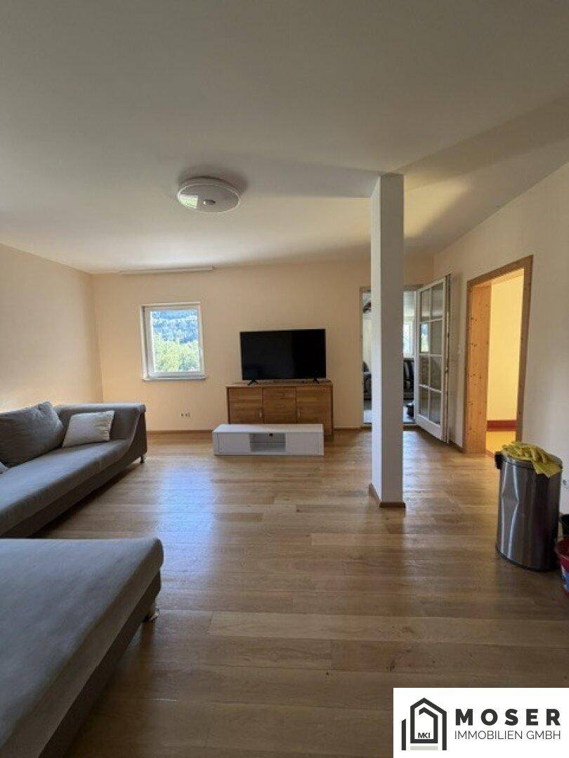 Helles Wohnzimmer mit großem Fernseher, Holzboden und offenem Grundriss, modern eingerichtet.