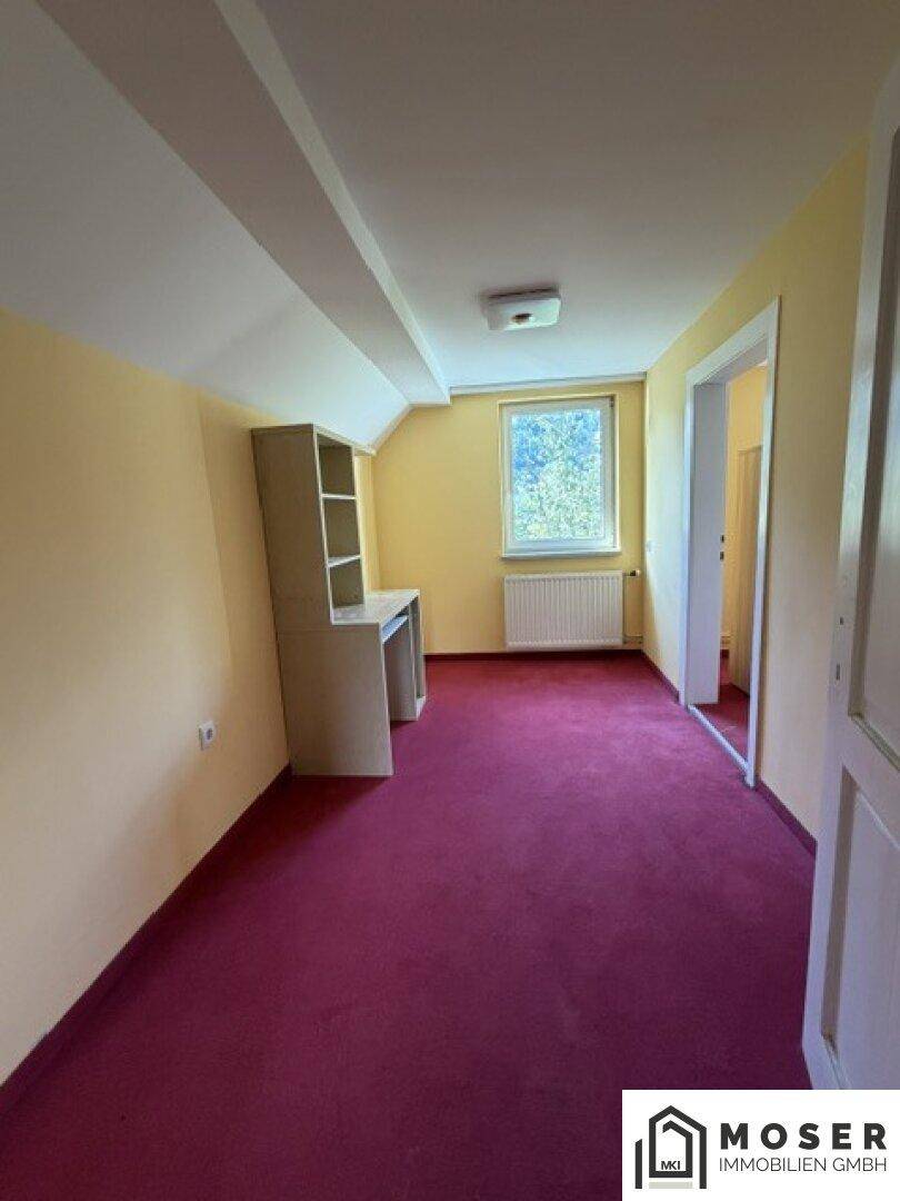Heller Raum mit rotem Teppichboden, Schreibtisch und Fenster unter der Dachschräge, ideal als Büro.