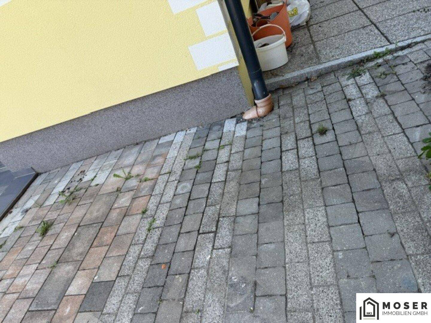 Detailansicht des gepflasterten Bereichs neben dem Haus mit Regenrinne und Entwässerung.