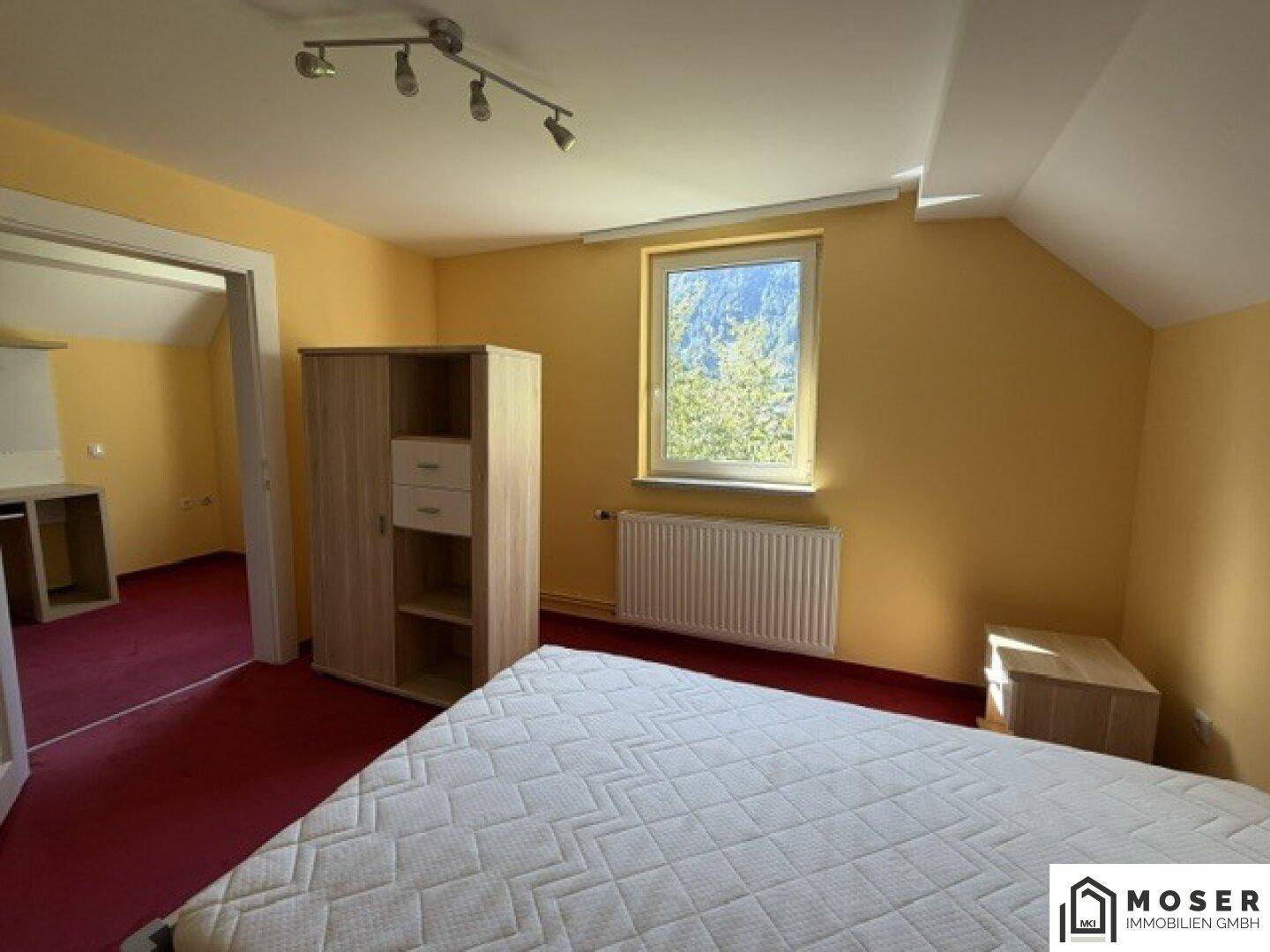Schlafzimmer mit Einzelbett, kleinem Schrank und rotem Teppichboden unter der Dachschräge.
