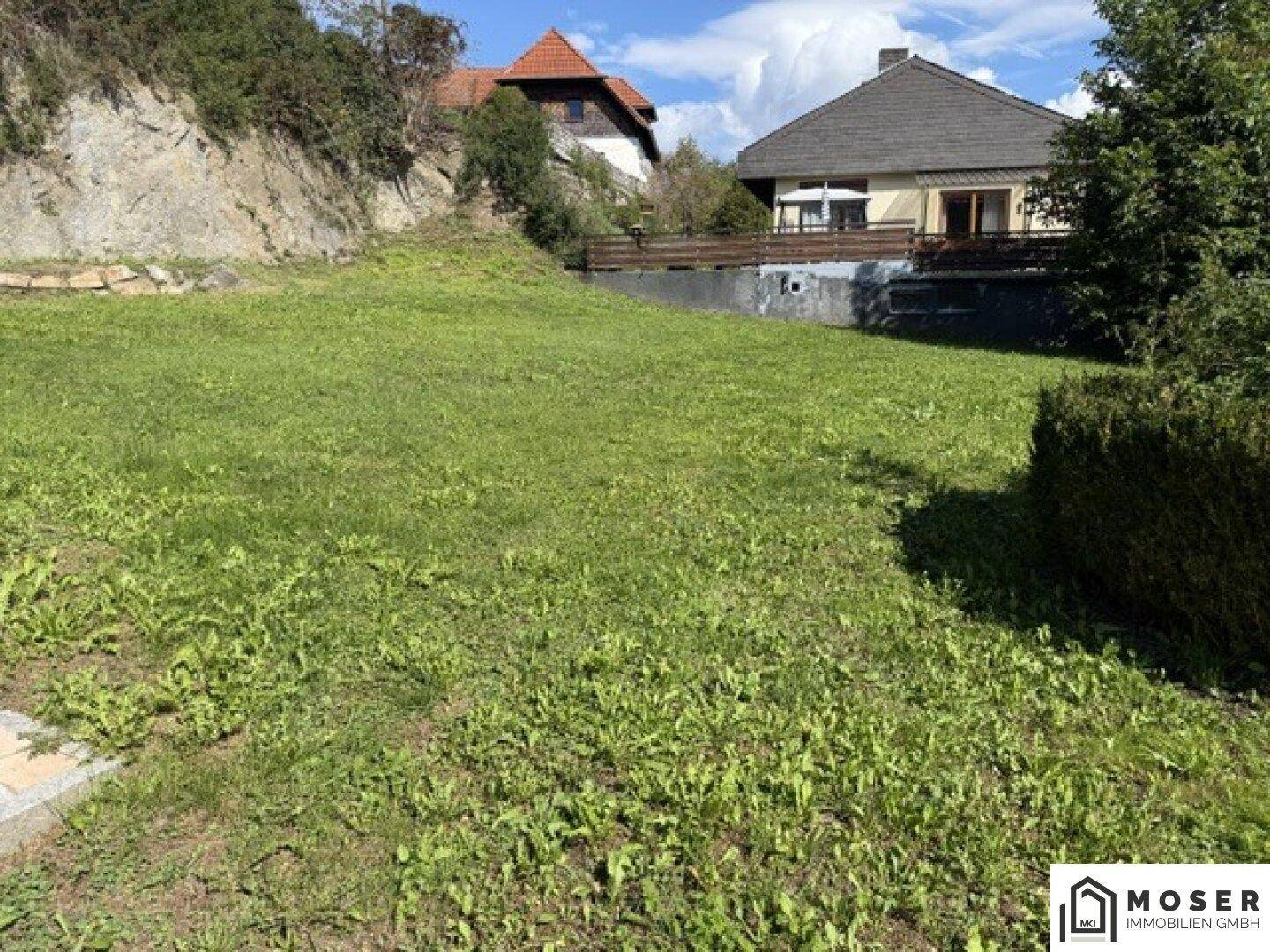 Großer Garten mit Rasenfläche und Hecke, umgeben von Natur und einem Einfamilienhaus mit Balkon.