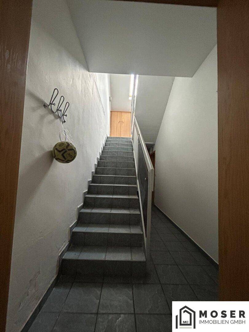Treppenhaus mit Fliesenstufen, weiß gestrichenen Wänden und einem Geländer.
