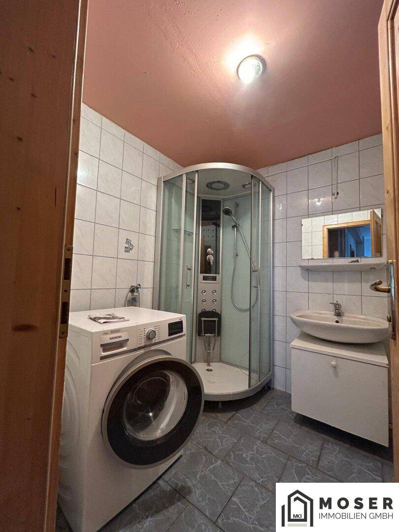 Badezimmer mit Duschkabine, Waschmaschine, Waschbecken und Fliesenboden.