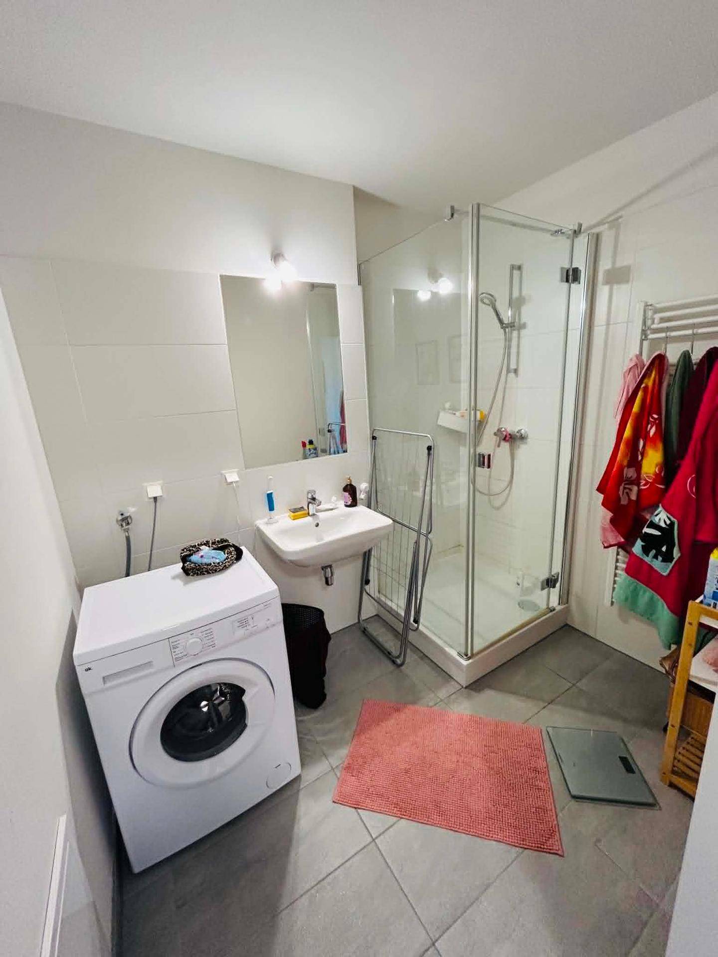 Modernes Badezimmer mit Dusche, Waschbecken und Waschmaschine, ausgestattet mit hellen Fliesen.