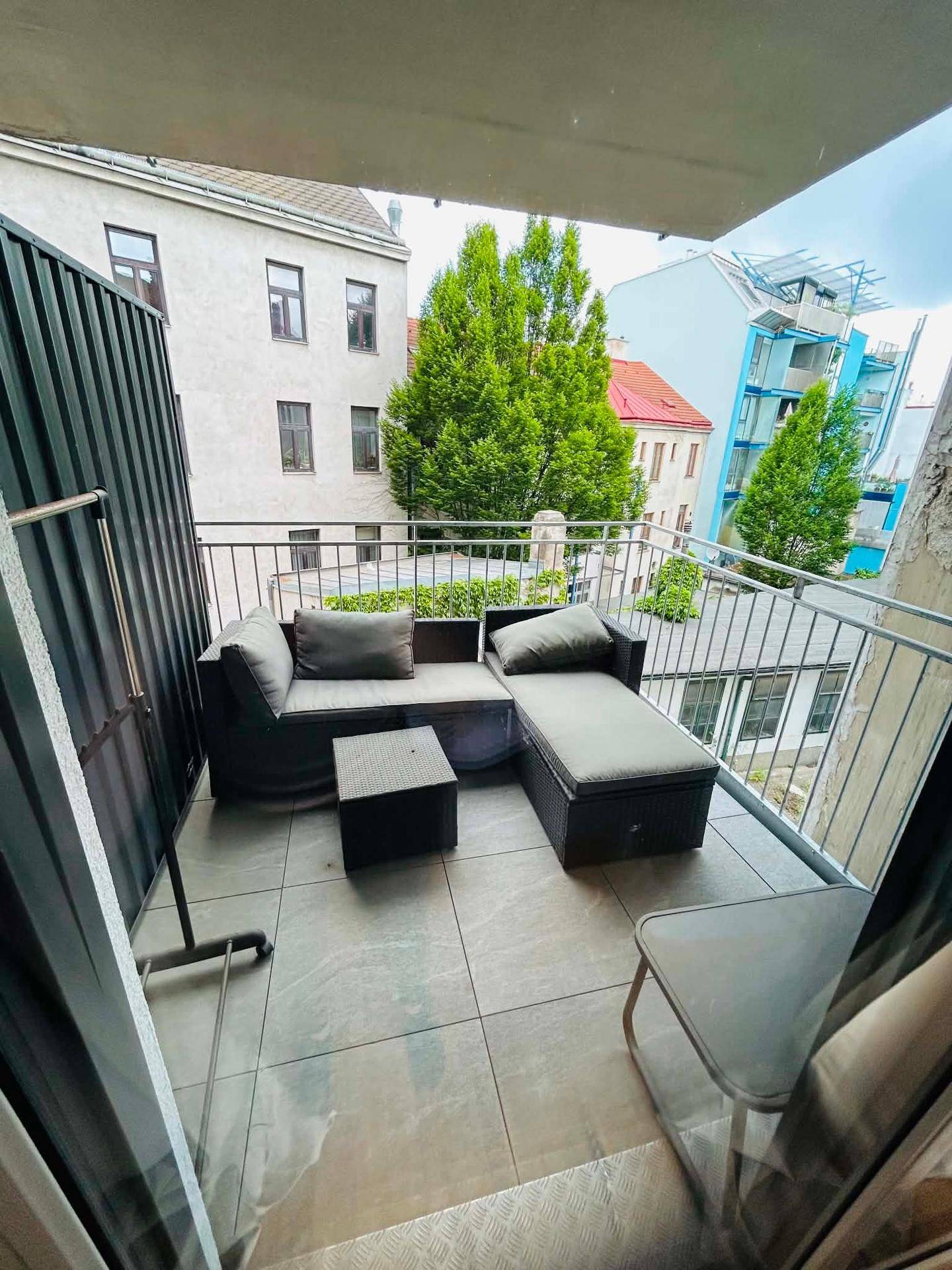 Kleiner Balkon mit Outdoor-Lounge-Möbeln und Blick auf die umliegenden Gebäude und Bäume.
