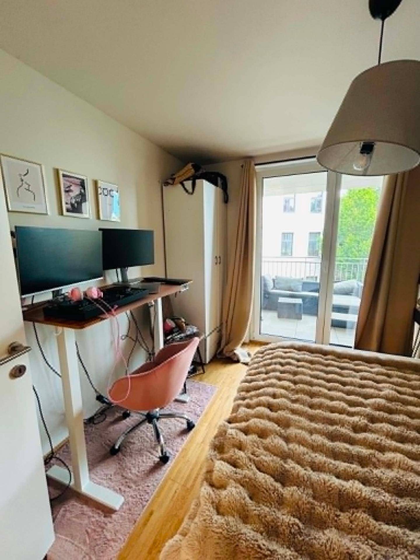 Schlafzimmer mit Bett, Schreibtisch und Zugang zu einem Balkon, hell und modern eingerichtet.