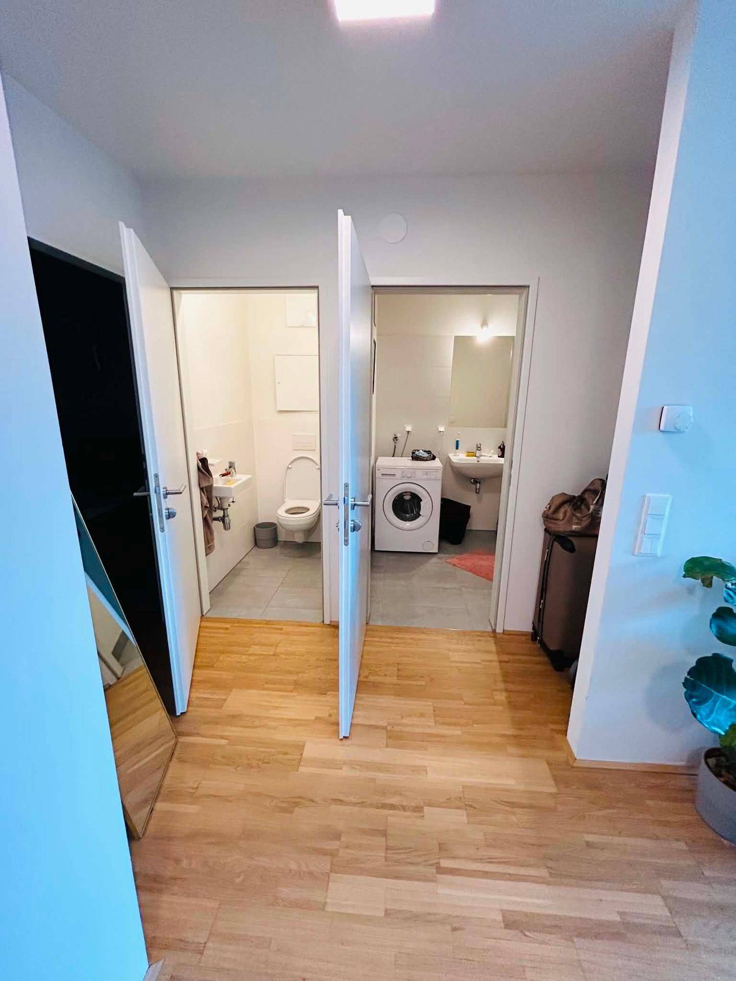 Heller Flur mit Holzboden und Zugang zu einem Badezimmer und einer separaten Toilette.