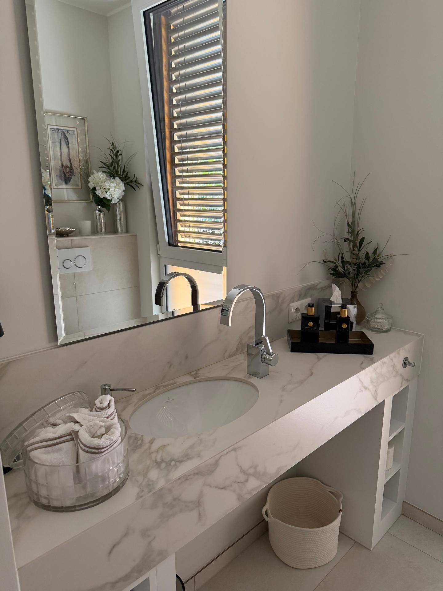 Modernes Badezimmer mit Marmorwaschtisch, großem Spiegel und Fenster für natürliches Licht.