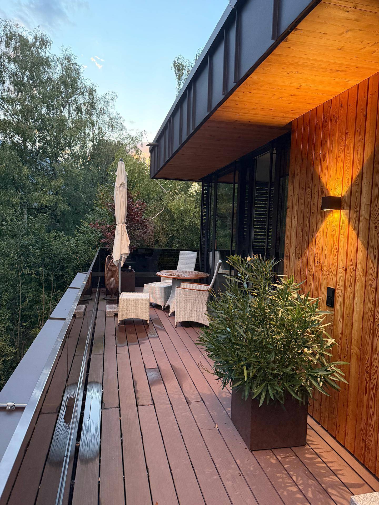 Geräumige Terrasse mit Holzverkleidung, bequemen Gartenmöbeln und Blick ins Grüne am Abend.