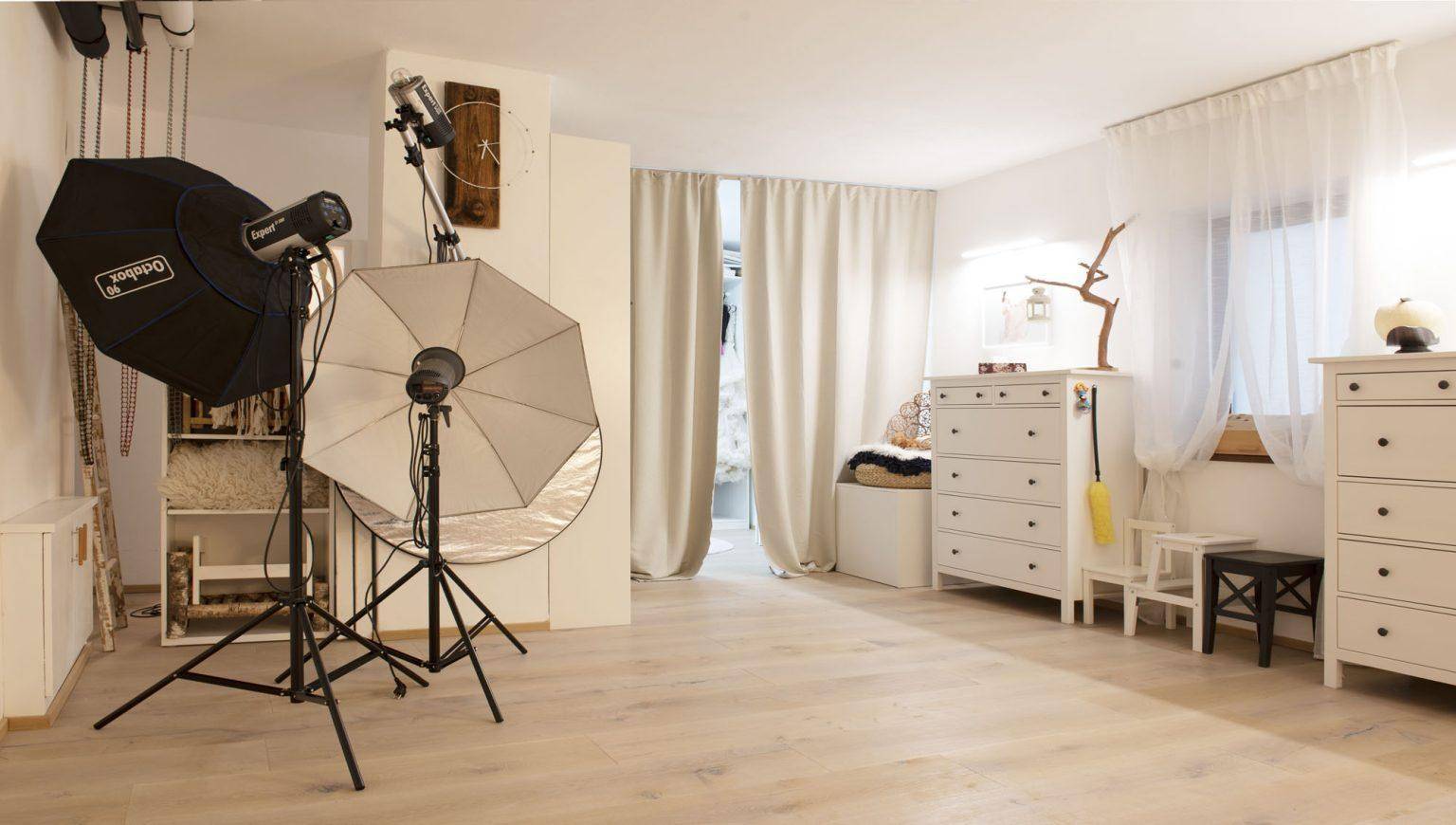 Geräumiges Fotostudio mit professioneller Beleuchtung und weißen Kommoden am Fenster.