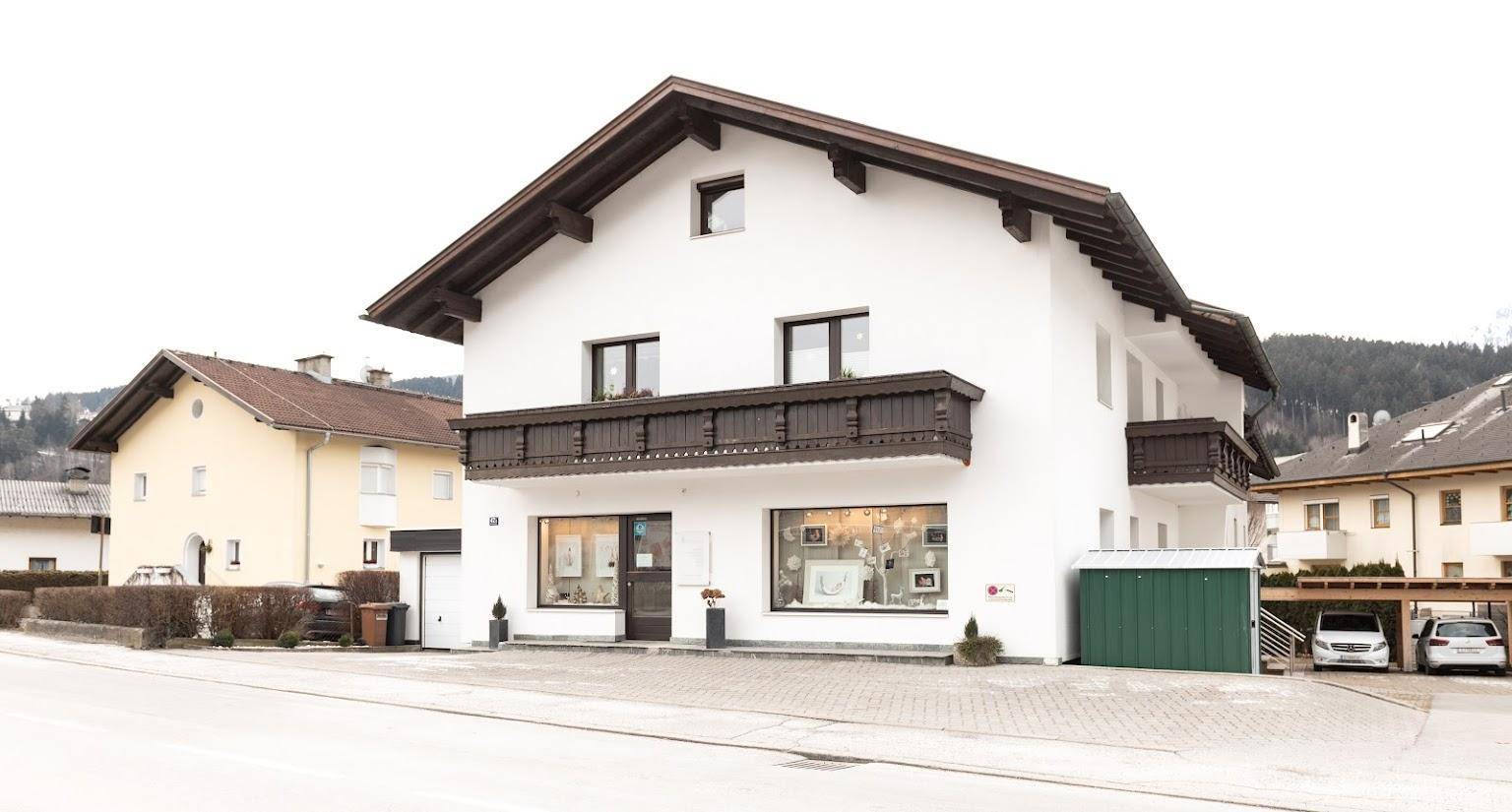 Traditionelles weißes Gebäude mit Holzbalkon, Ladenfront im Erdgeschoss und grüner Garage.