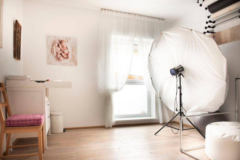 Heller Raum mit großem Fenster, Wickeltisch und professioneller Fotobeleuchtung.