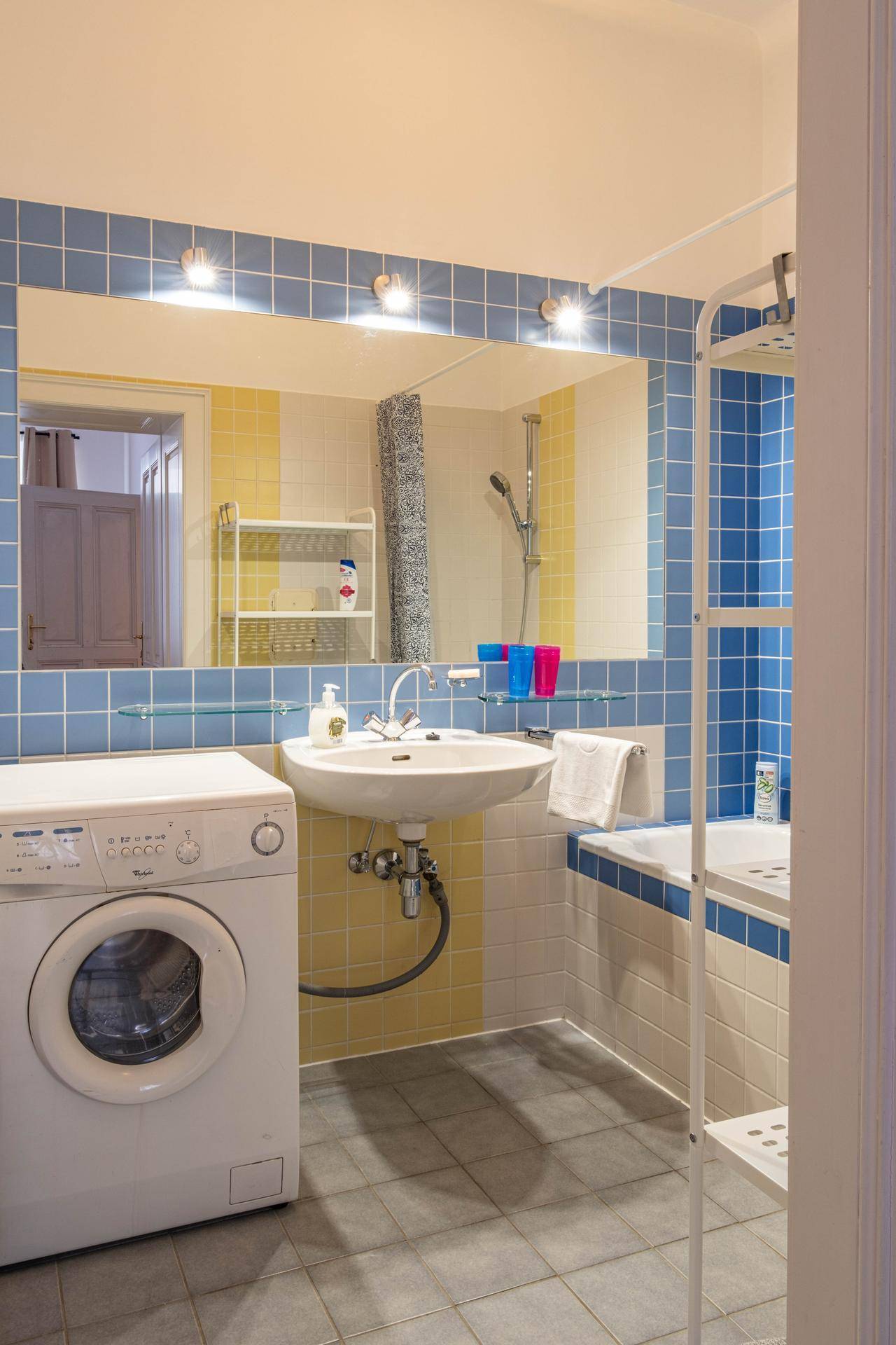 Badezimmer mit Waschmaschine, Waschbecken und farbigen Fliesen in Blau und Gelb, typisch für die 80er Jahre.