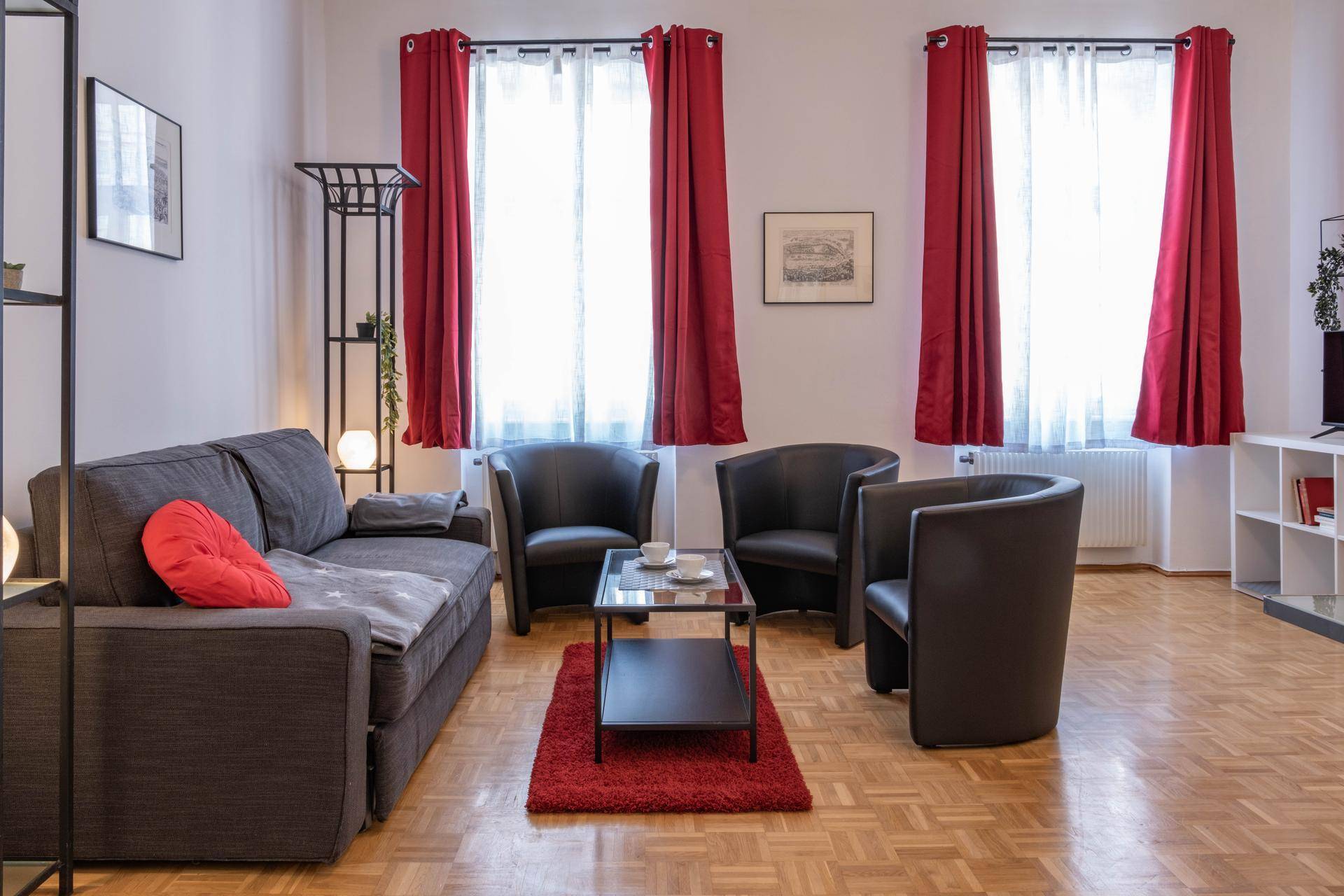 Gemütliches Wohnzimmer mit Sofa, Sesseln, Couchtisch und Parkettboden, durch große Fenster gut beleuchtet.