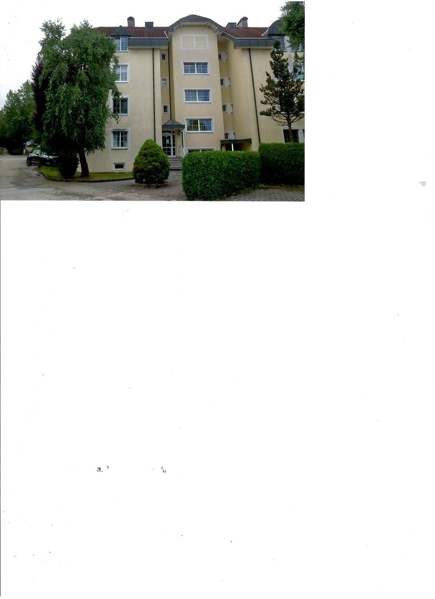 Mehrstöckiges Wohngebäude mit gepflegter Fassade, umgeben von Bäumen und Hecken.