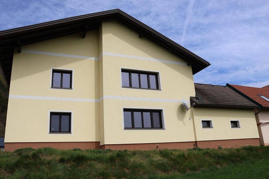 Seitenansicht eines gelben Einfamilienhauses mit braunen Fenstern und Satteldach in ländlicher Umgebung.