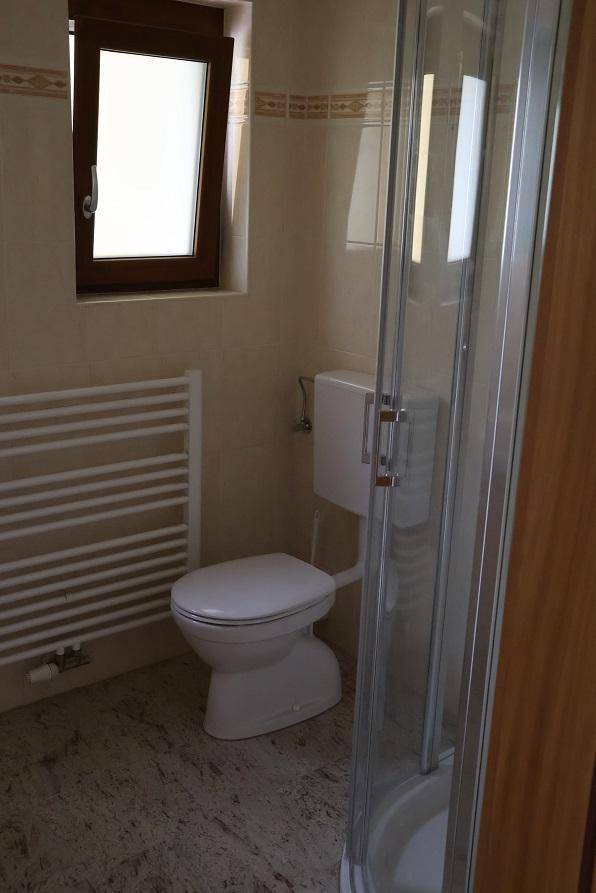 Badezimmer mit Duschkabine, Toilette, Fenster und beheiztem Handtuchhalter.