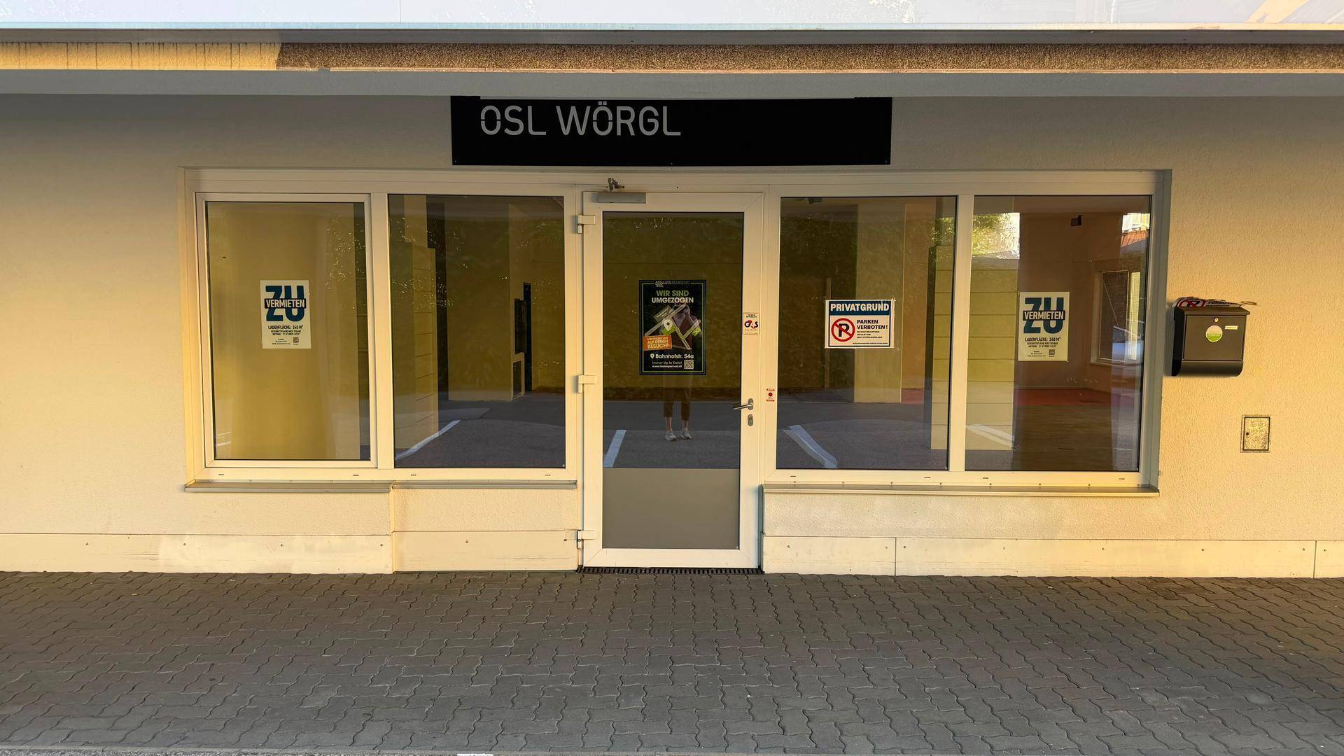 Eingangsbereich eines Geschäfts mit großen Glasfenstern und einer Glastür, die viel Tageslicht hereinlässt.