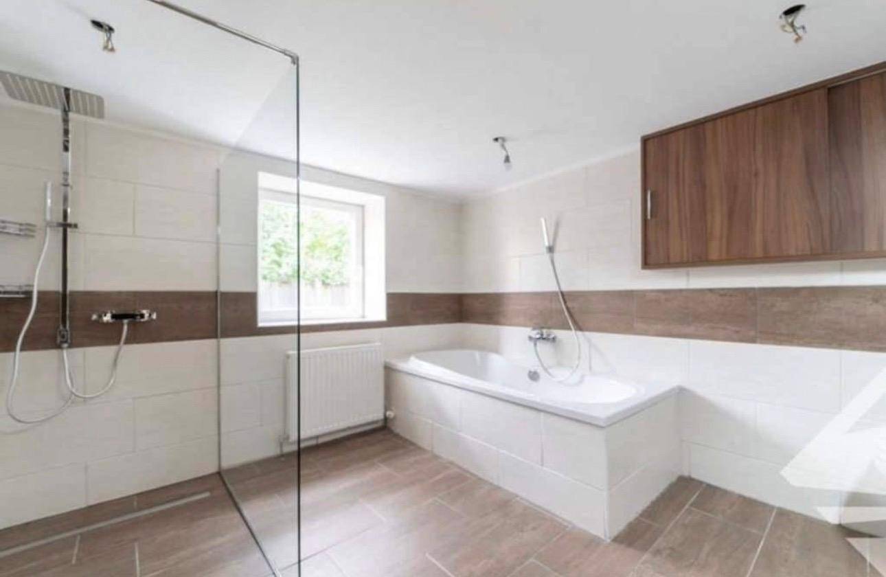 Geräumiges Badezimmer mit Badewanne, großer Dusche und Fenster, ausgestattet mit modernen Fliesen.