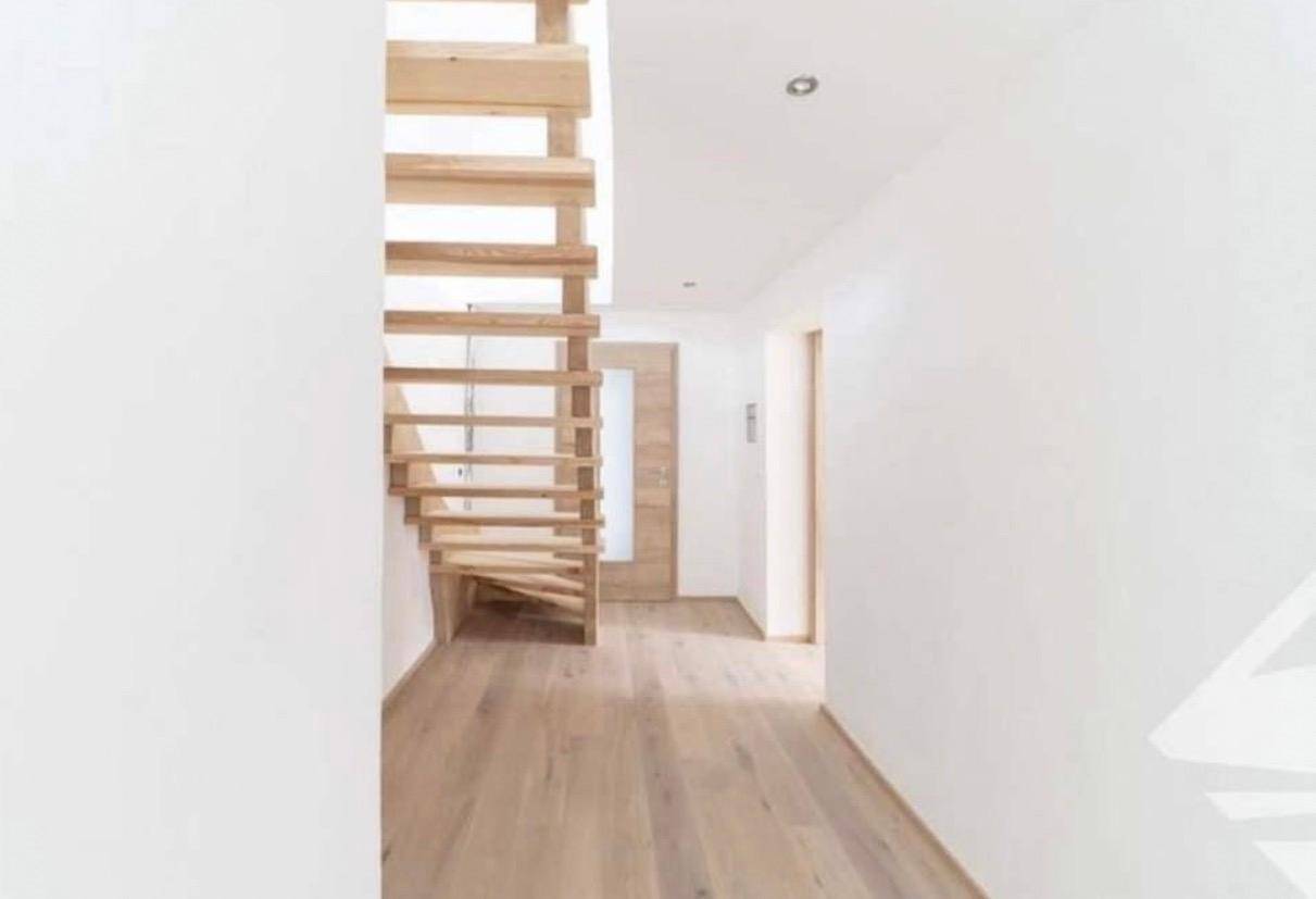 Heller Flur mit offener Holztreppe und Holzboden, der verschiedene Ebenen des Hauses verbindet.
