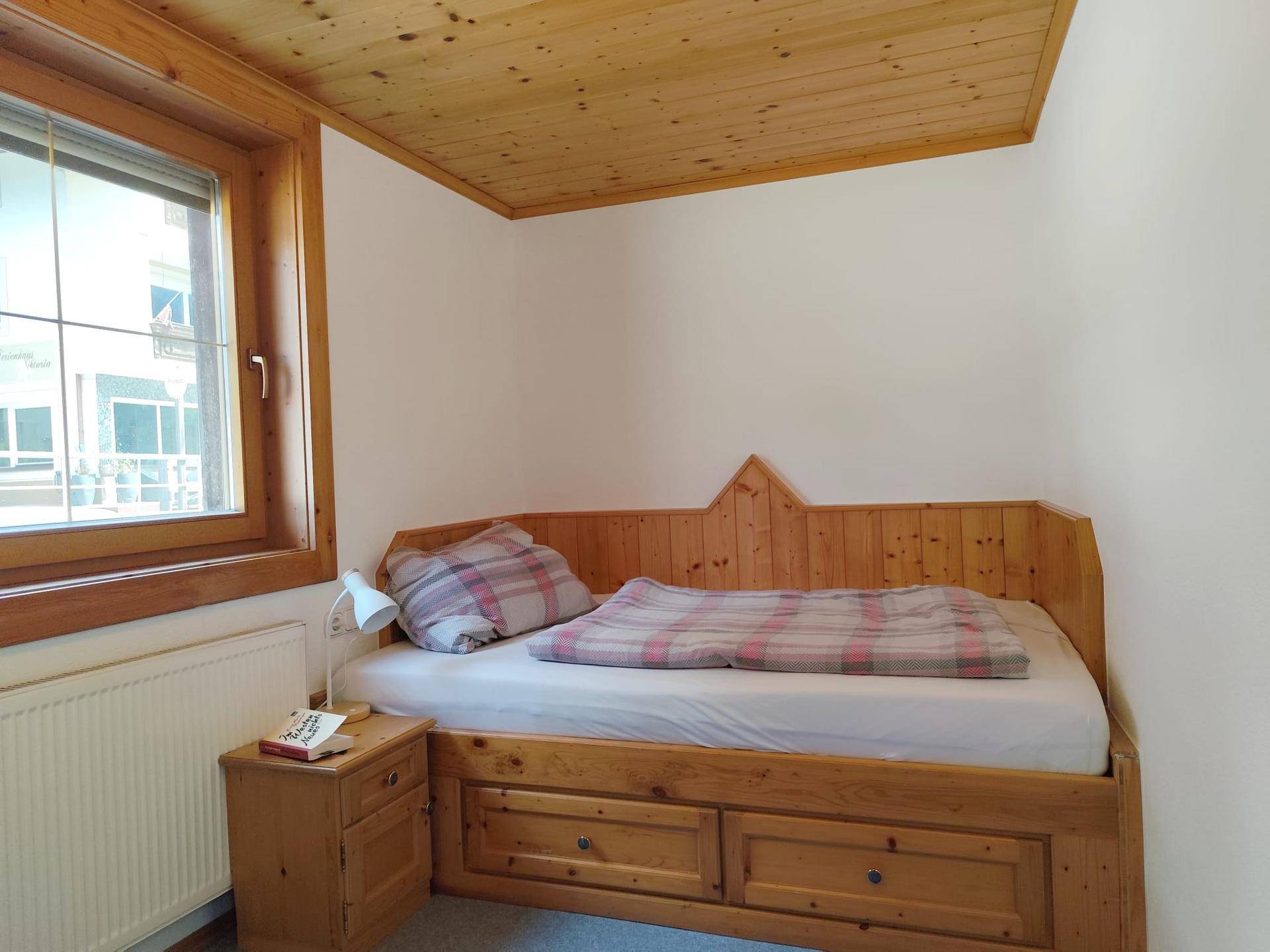 Kinderzimmer mit Holzbett, Nachttisch und Fenster mit Blick nach draußen.