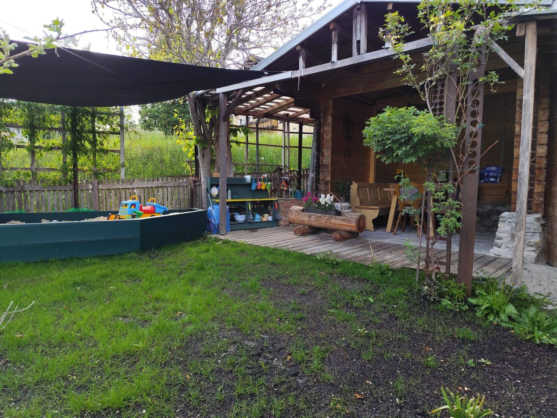 Garten mit Sandkasten, überdachtem Sitzbereich und rustikalem Holzschuppen.