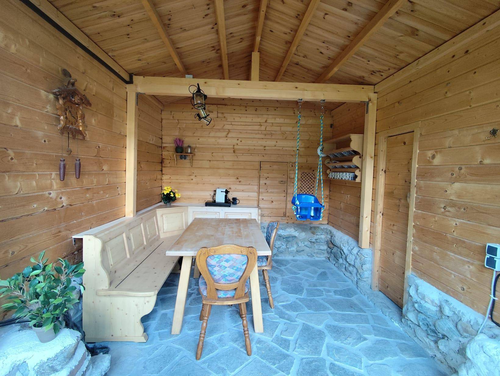 Überdachter Außenbereich mit Holztisch, Bänken und rustikalem Steinboden.