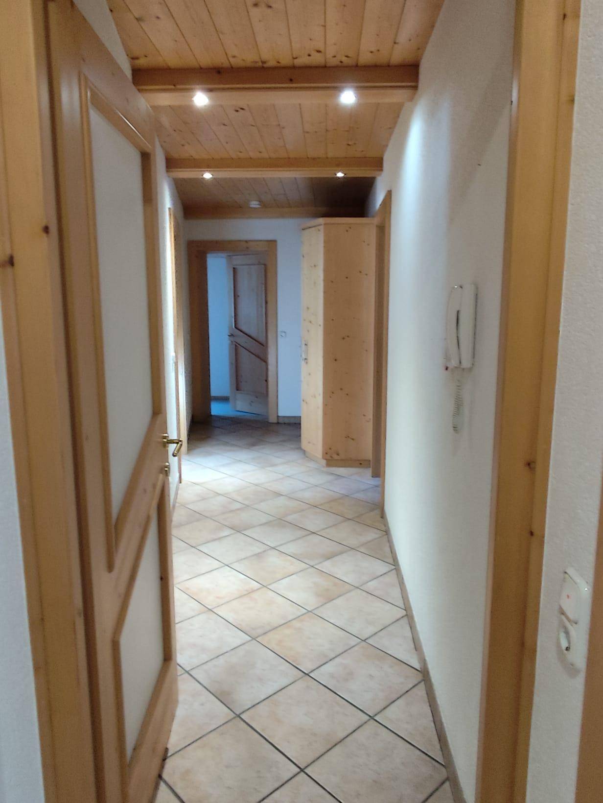 Langer Flur mit Holztüren, Fliesenboden und einer warmen Holzdeckenverkleidung.