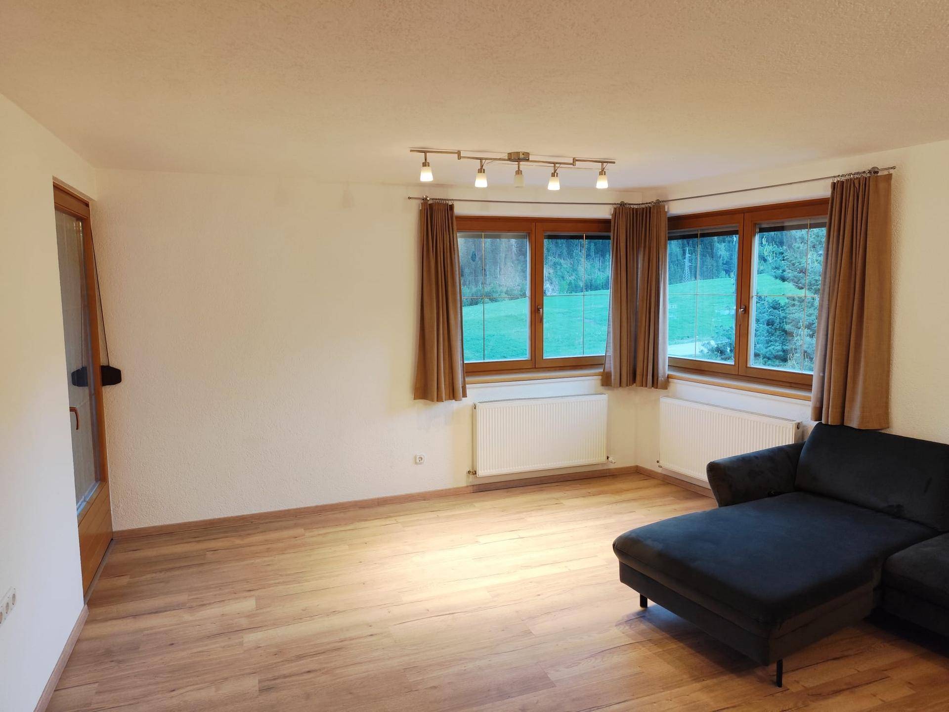 Geräumiges Wohnzimmer mit Holzboden, großen Fenstern und Blick ins Grüne.
