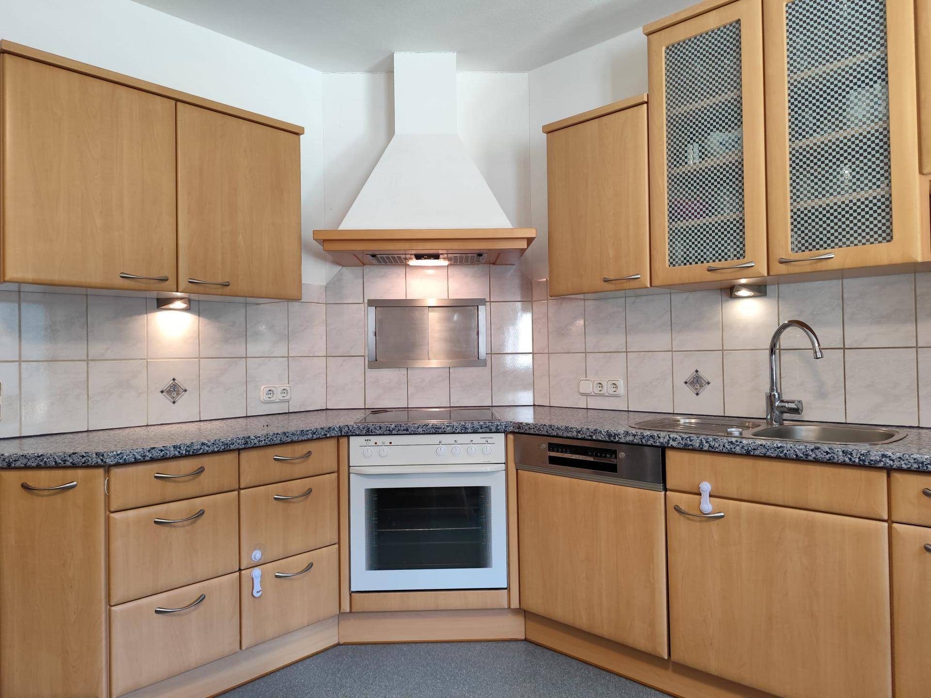 Funktionale Küche mit Holzschränken, integrierten Geräten und heller Fliesenrückwand.