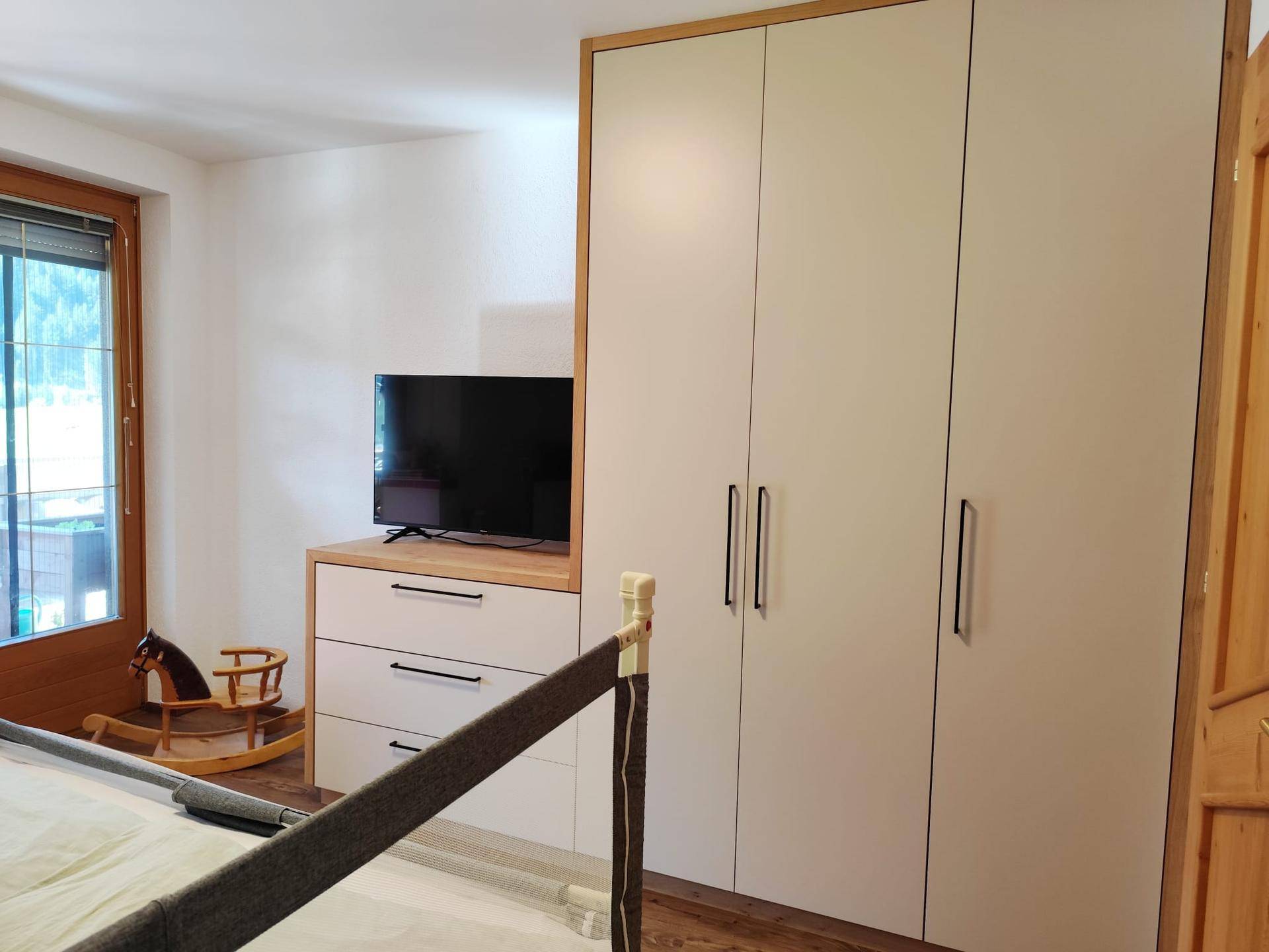 Schlafzimmer mit modernem Kleiderschrank, Kommode und warmem Holzboden.
