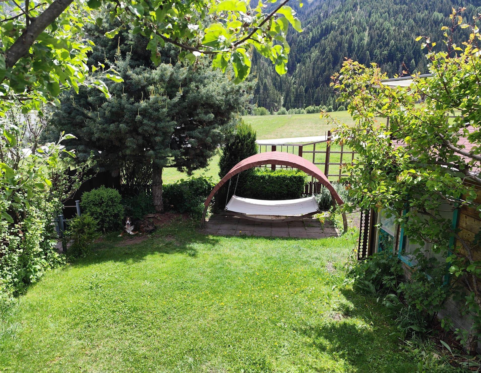 Grüner Gartenbereich mit Schaukel, Bäumen und malerischem Bergblick im Hintergrund.