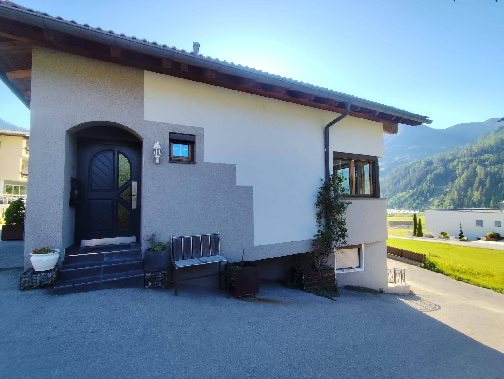 Eingangsbereich des Hauses mit dunkler Tür, seitlichem Zugang und Bergblick im Hintergrund.