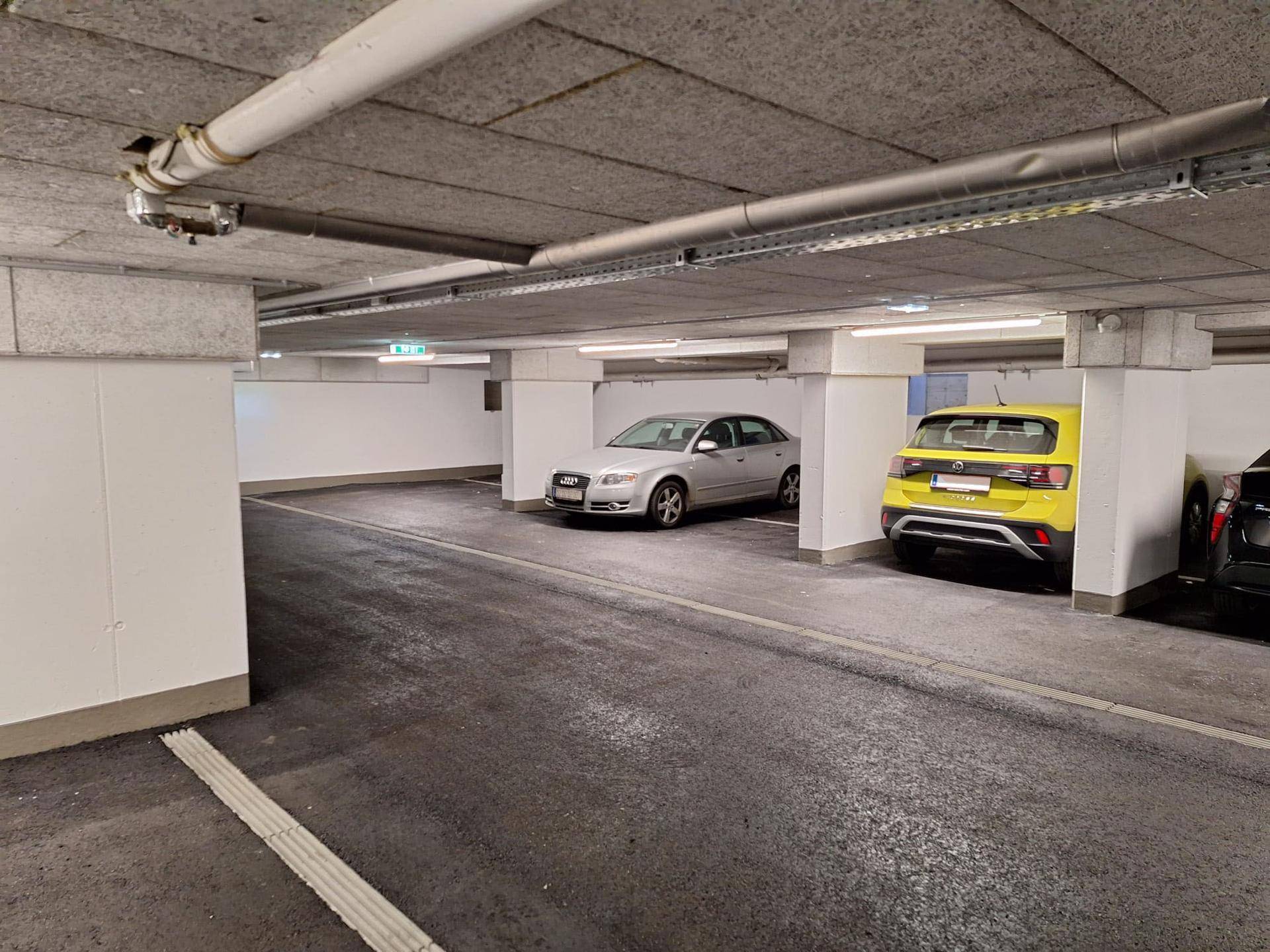 Geräumige Tiefgarage mit sauberem Betonboden und sichtbaren Installationen an der Decke.