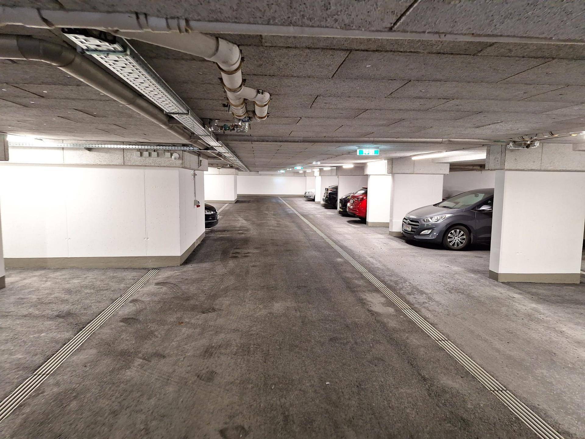 Lange Tiefgaragenzufahrt mit mehreren geparkten Fahrzeugen und klarer Fahrbahnmarkierung.