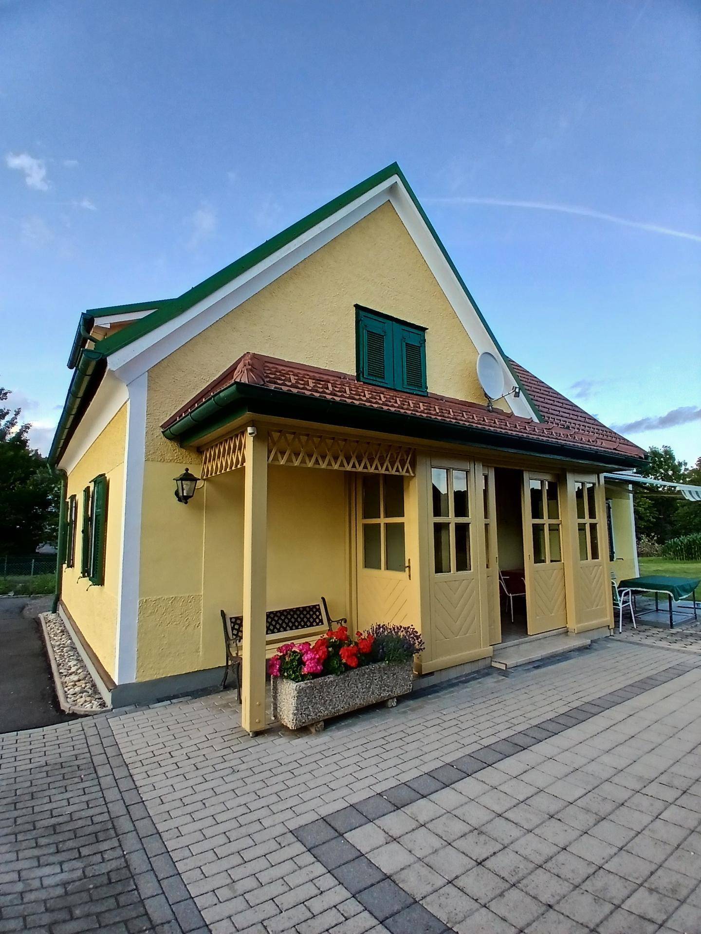 Charmantes gelbes Haus mit überdachtem Eingangsbereich, Blumenkasten und gepflastertem Vorplatz.