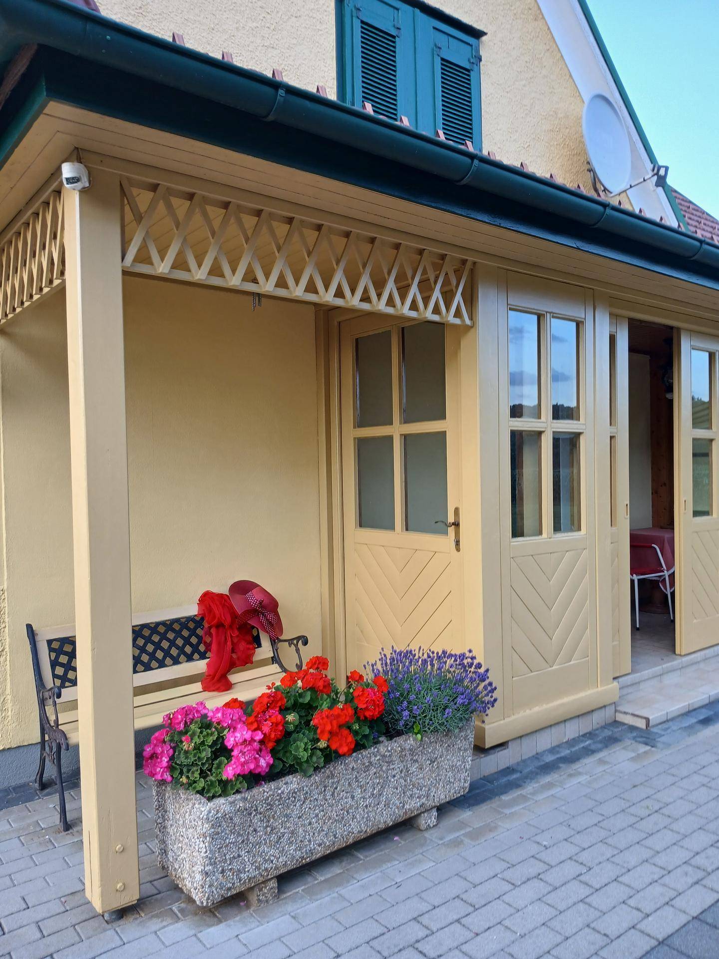 Detailansicht des Hauseingangs mit einer Bank, bunten Blumen und traditionellen Holzelementen.