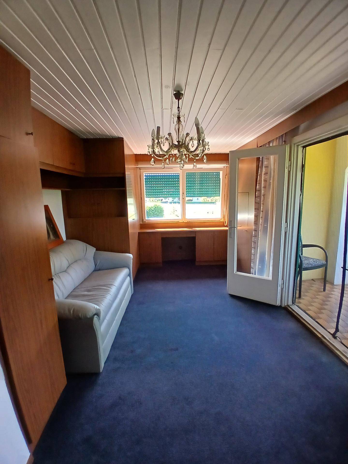 Schlafzimmer mit blauem Teppichboden, Holzmöbeln und direktem Zugang zu einem Balkon.